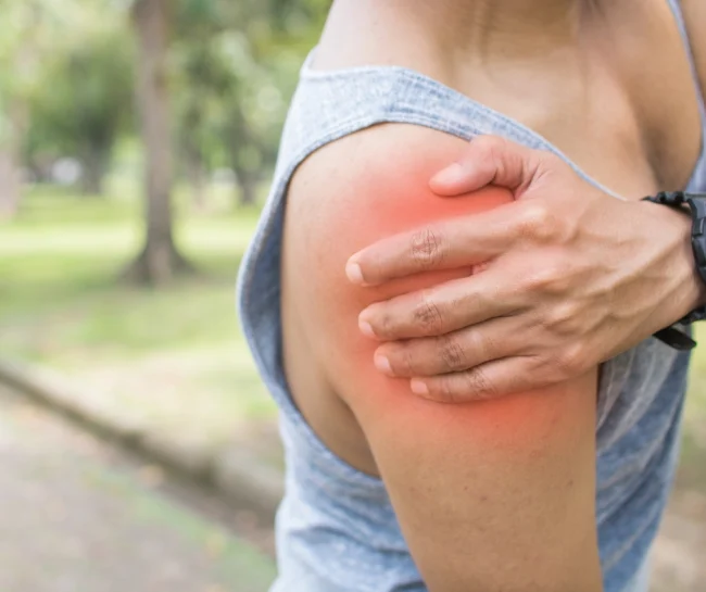 A person in a sleeveless shirt holding their shoulder, with a visible red area indicating pain or inflammation, suggesting a possible rotator cuff injury.